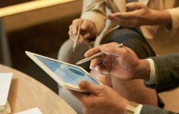 Dwie osoby siedzą z tabletem, pokazują coś długopisem na ekranie