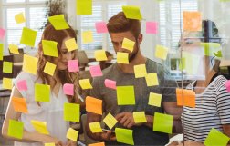 dwie osoby stoją przy przezroczystej tablicy z karteczkami