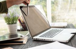 Dłonie z długopisami wskazującymi coś na otwartym laptopie