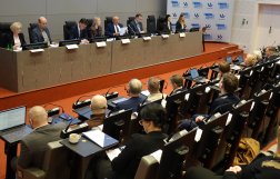 Na zdjęciu widać osiem osób zasiadających przy stole prezydialnym i kilkanaście osób siedzący na widowni. W tle ścianka Funduszy Europejskich