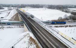 Na zdjęciu widok z lotu ptaka na zaśnieżony wiadukt, a pod nim przejeżdża pociąg