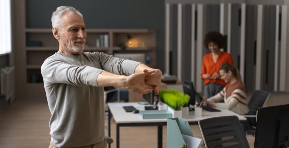 Starszy mężczyzna wykonuje ćwiczenia w biurze