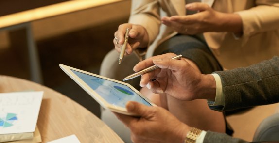 Dwie osoby siedzą z tabletem, pokazują coś długopisem na ekranie