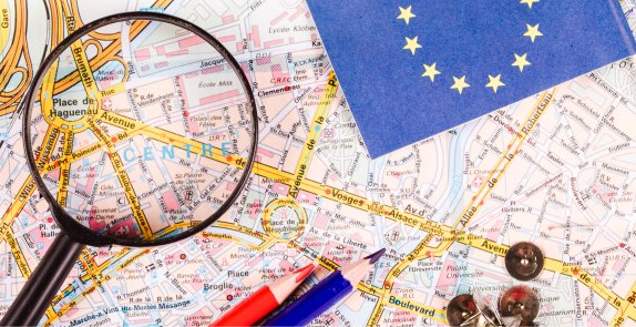 lupa, kredki i chorągiewka z flagą Unii Europejskiej połozone na mapie