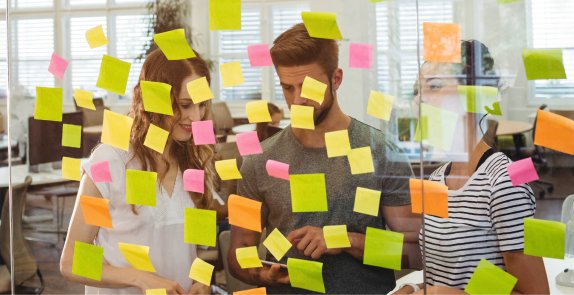 dwie osoby stoją przy przezroczystej tablicy z karteczkami