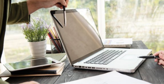 Dłonie z długopisami wskazującymi coś na otwartym laptopie
