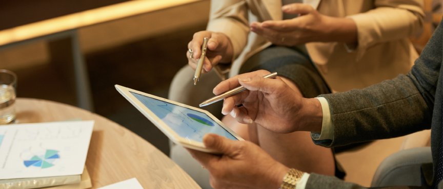 Dwie osoby siedzą z tabletem, pokazują coś długopisem na ekranie