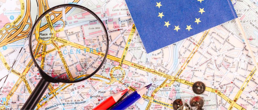 lupa, kredki i chorągiewka z flagą Unii Europejskiej połozone na mapie