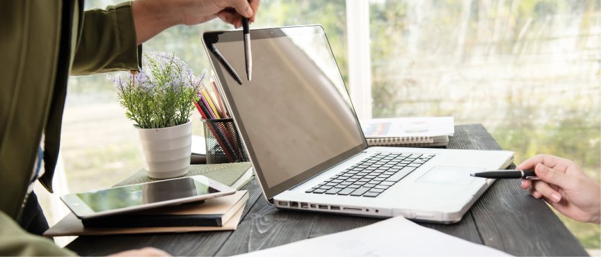 Dłonie z długopisami wskazującymi coś na otwartym laptopie